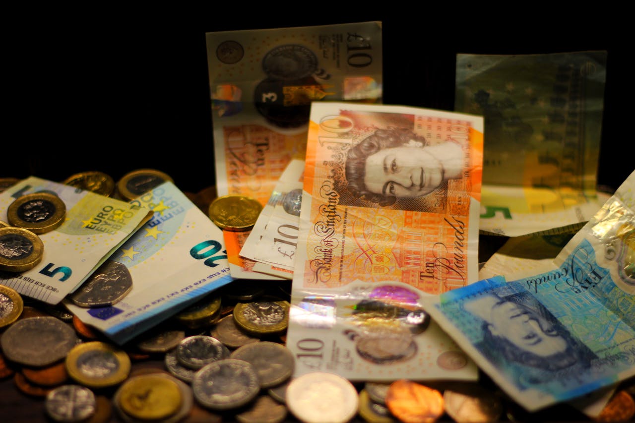 A dark-toned close-up of various Euro and Pound banknotes and coins scattered.